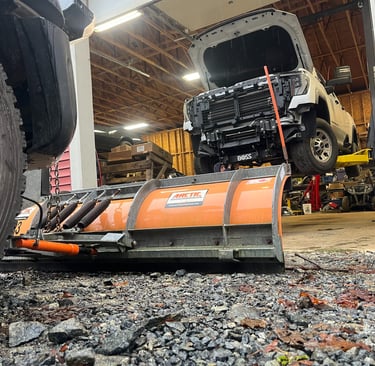 looking into a shop bay with a truck on a hoist from behind a plow blade