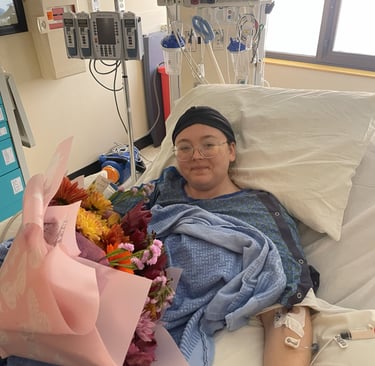 Baylie Phillips in hospital bed with flowers on her lap and ICU machines in the background.