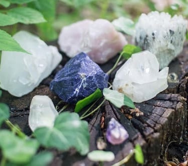 Cristales curativos en bruto, como cuarzo rosa y lapislázuli, sobre un tronco de madera.