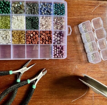 Materiales para la elaboración de joyería, cuentas organizadas en una caja, pinzas y alambre.