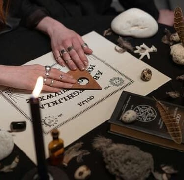 Manos sobre una tabla ouija en una sesión espiritual iluminada por velas.