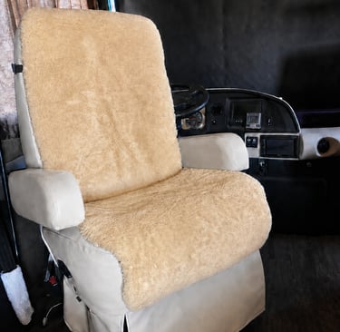 Beige sheepskin seat cover installed on a swivel captain chair inside a luxury RV motorhome cabin.