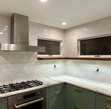 Modern kitchen with white subway tile backsplash, green cabinets, and stainless steel range hood.