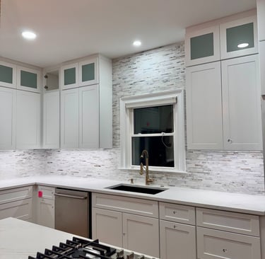 Modern white kitchen with shaker cabinets, gold faucet, and stone tile backsplash.