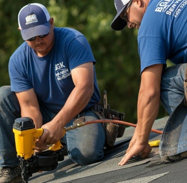 Professional roofing contractors installing asphalt shingles on a residential roof using a pneumatic nail gun.