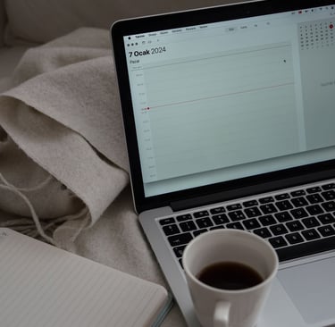 Notebook aberto sobre um sofá com calendário exibido na tela, ao lado de uma xícara de café e um cad
