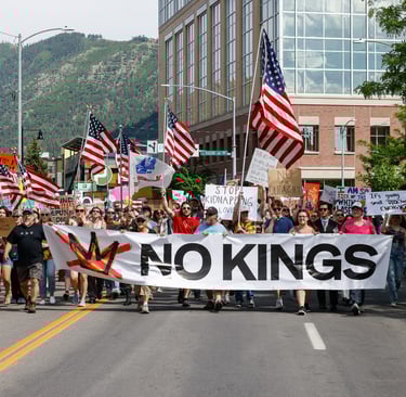 Protesters march through a city street holding a large No Kings banner and American flags during a political rally.