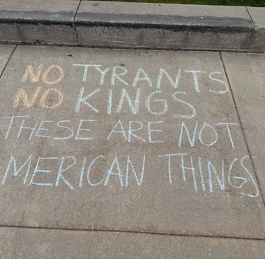 Sidewalk chalk art protest message reading No Tyrants No Kings These Are Not American Things.