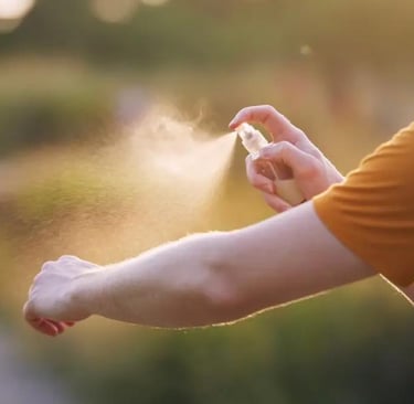 Una persona se aplica repelente de insectos en el brazo al aire libre, al atardecer.
