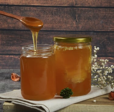 Pure organic honey dripping from a wooden spoon into glass jars on a rustic table.
