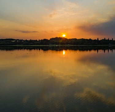 Coucher de soleil doré se reflétant sur un lac calme, avec la silhouette des arbres et des nuages.