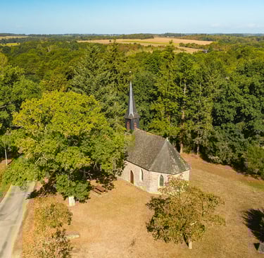 Vue aérienne d'une chapelle historique en pierre avec une flèche noire nichée dans un paysage forest
