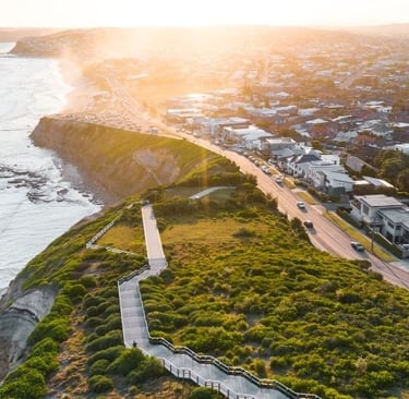 Scenic view of Bathers Way in Newcastle with a cliffside path, ocean waves, and golden sunset light over the coastline.