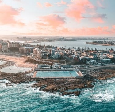 Aerial sunset view of Newcastle’s coastline with the ocean pool, beach, and city skyline.