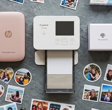 Flat lay of Canon Ivy, HP Sprocket and 3 other portable sticker printers surrounded by photo stickers.
