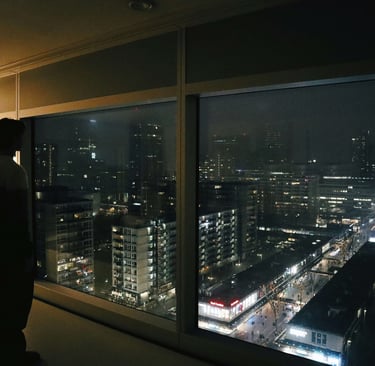 Silhouette of a person looking at the glowing city skyline and urban buildings at night through a large window.