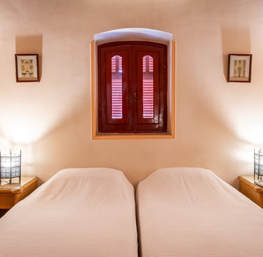villa bedroom featuring twin beds, ornate metal lanterns, and a red arched window shutter.