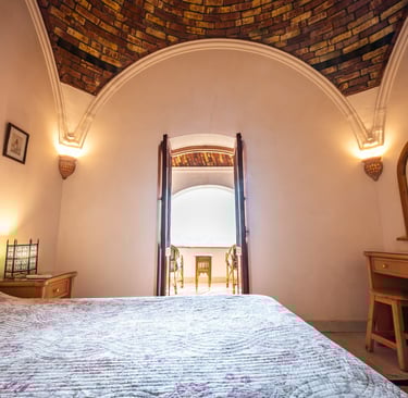 Rustic bedroom with a vaulted brick ceiling, wooden vanity, and balcony view.