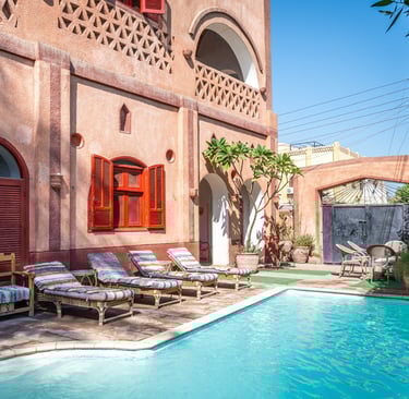Luxury terracotta villa courtyard featuring a turquoise swimming pool and striped lounge chairs.
