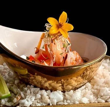 Gourmet shrimp ceviche appetizer served in a gold bowl with edible flowers and sprouts over sea salt.
