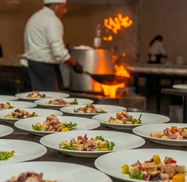 Professional chef preparing gourmet octopus salad plates in a restaurant kitchen with a stove fire.