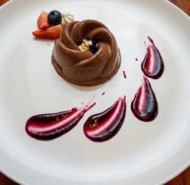 Gourmet chocolate mousse dessert with berry coulis, fresh strawberries, and gold leaf garnish on a white plate.
