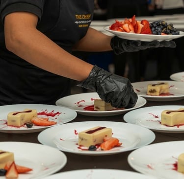 Professional chef plating gourmet desserts with fresh strawberries and berry sauce for event catering.
