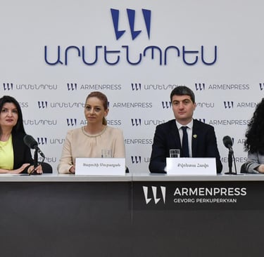 Four panelists seated at a table during an Armenpress news conference with microphones and nameplates.