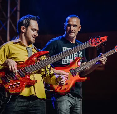 Two guitarists performing on stage with matching red guitars under blue stage lights.