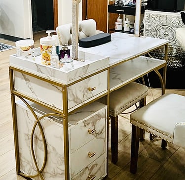 Elegant marble and gold manicure table with desk lamp, storage drawers, and matching white nail technician chairs.