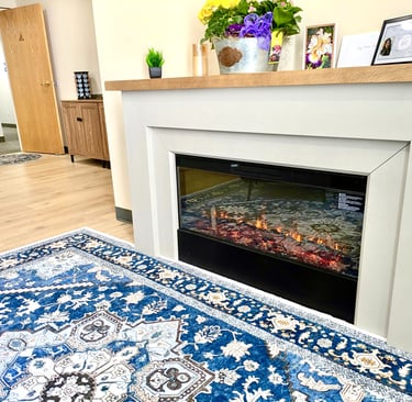 Modern electric fireplace with white mantel and blue patterned area rug in a cozy office waiting room.