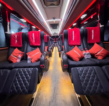 Luxury bus interior featuring reclining black leather seats with red pillows and ambient led lighting.