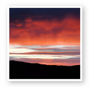 Stunning sunset sky with vibrant red, orange, and dark blue clouds above a silhouetted mountain range, enhancing