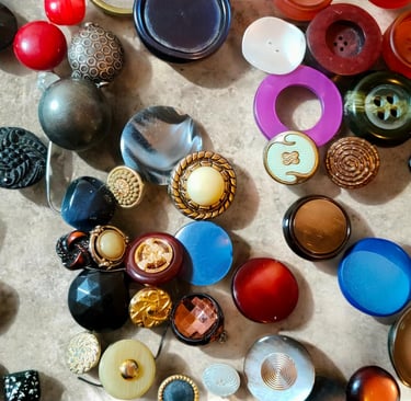 A colorful collection of vintage sewing buttons in various sizes, textures, and materials spread across a surface.