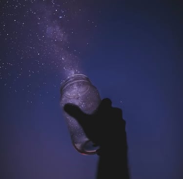 Silhouette of a hand holding a glass jar catching a purple Milky Way galaxy and stars.