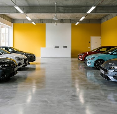 Modern car showroom with rows of new vehicles parked on a polished concrete floor against a yellow accent wall.