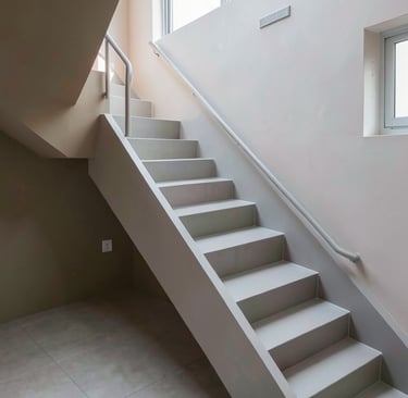 Modern minimalist white indoor staircase with metal handrails and neutral plaster walls.