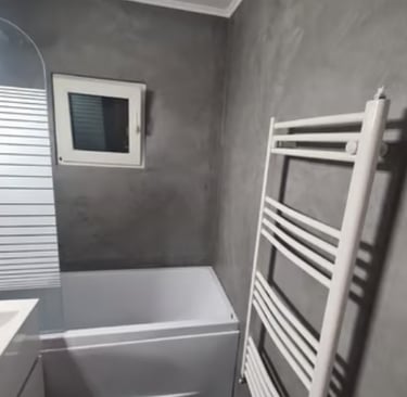 Casa de banho moderna com paredes em microcimento cinzento, banheira branca e toalheiro aquecido.