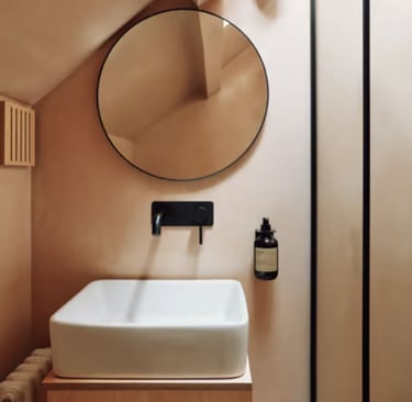 Modern bathroom with beige microcement walls, white washbasin, black wall-mounted tap and round mirr