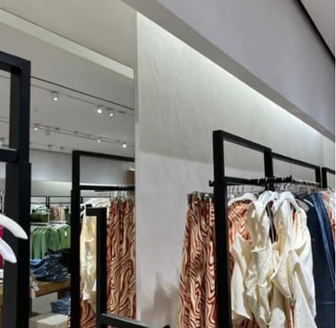 Modern clothing store display featuring patterned skirts and white tops on black retail racks.