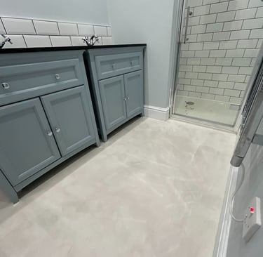 Modern bathroom with microcement flooring and walls, double blue cabinets and walk-in shower with wh