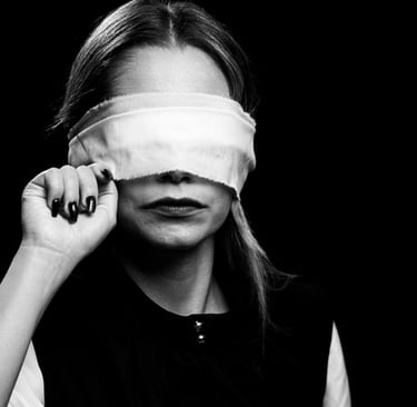 Kobieta z opaską na oczach w czarno-białym ujęciu, unosząca ją delikatnie palcami w kierunku światła