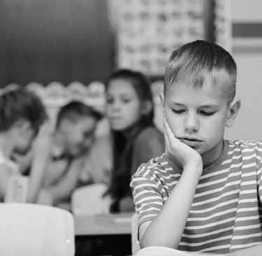 Chłopiec opierający głowę na dłoni, z poważnym, smutnym wyrazem twarzy i spuszczonym wzrokiem.