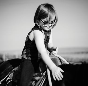 Dziewczynka w okularach siedzi na kucu. Dłonią dotyka jego grzywy.