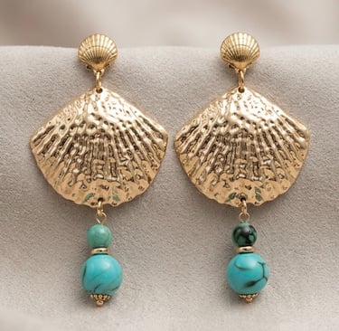 Gold seashell drop earrings with turquoise beads hanging on a neutral textured background.