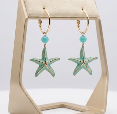 Gold hoop earrings with turquoise starfish charms and blue beads on a jewelry display stand.