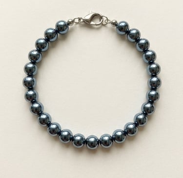 Polished dark grey hematite bead bracelet with a silver lobster claw clasp on a cream background.