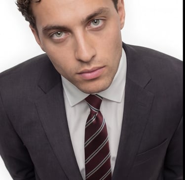 Professional young man with curly hair wearing a dark charcoal business suit and striped burgundy tie.