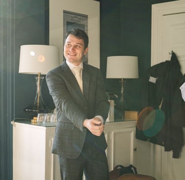 Groom smiling while making final adjustments to his shirt sleeves during wedding morning preparation