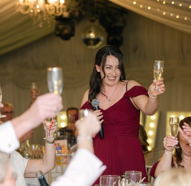 Bridesmaid in a red dress raising a glass to the couple at The Mill House Hotel